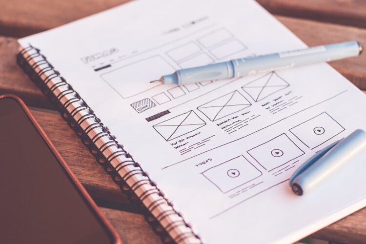 Schets van een nieuwe website met wireframes en pennen op een notitieblok naast een smartphone
