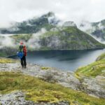 Wandelaar met outdooruitrusting kijkt uit over bergmeer in mistige omgeving