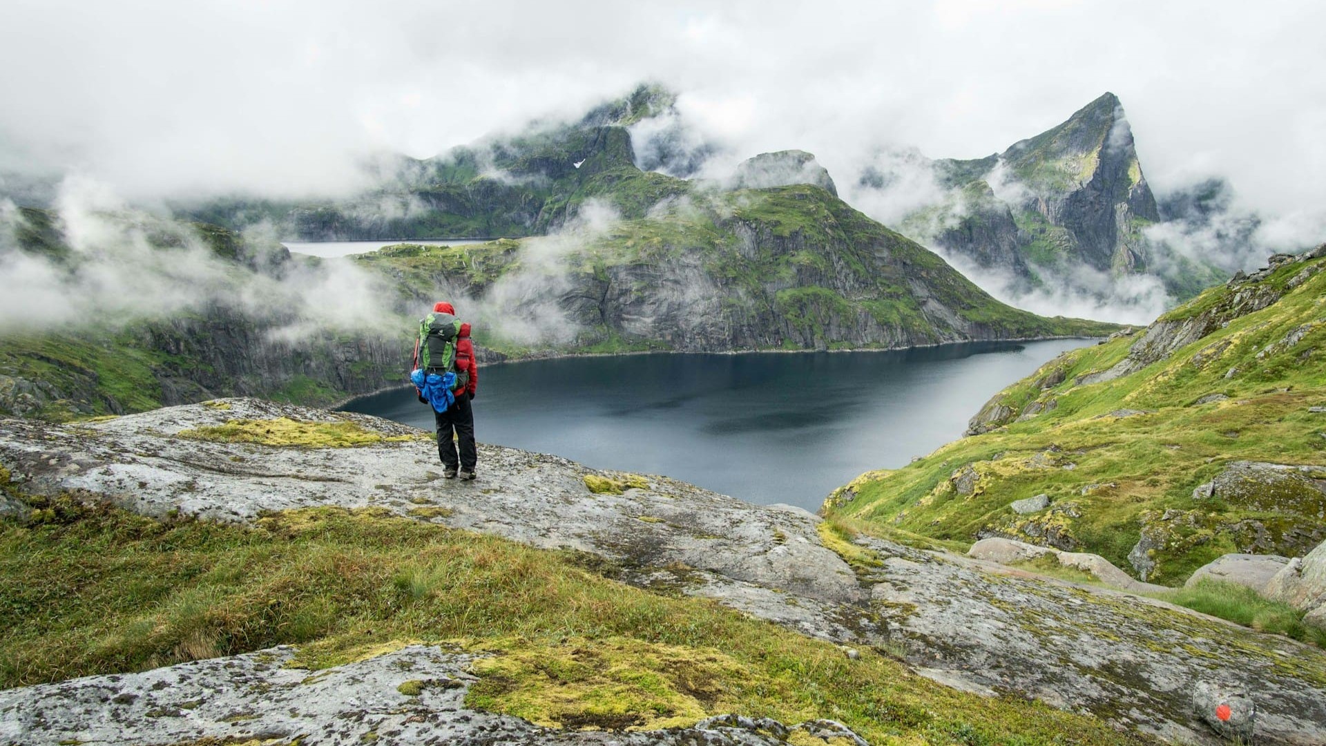 Wandelaar met outdooruitrusting kijkt uit over bergmeer in mistige omgeving