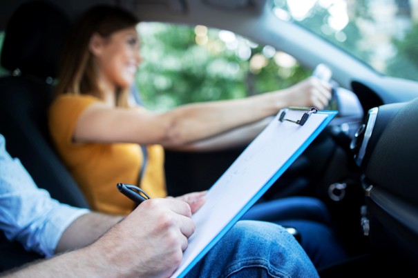 Rijinstructeur schrijft op een klembord terwijl een leerling achter het stuur van de auto zit.